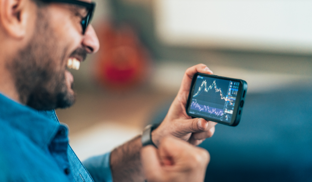 Homem feliz analisando gráficos financeiros no celular.