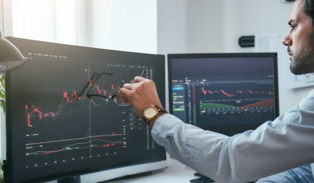 Homem analisando gráficos em dois monitores.