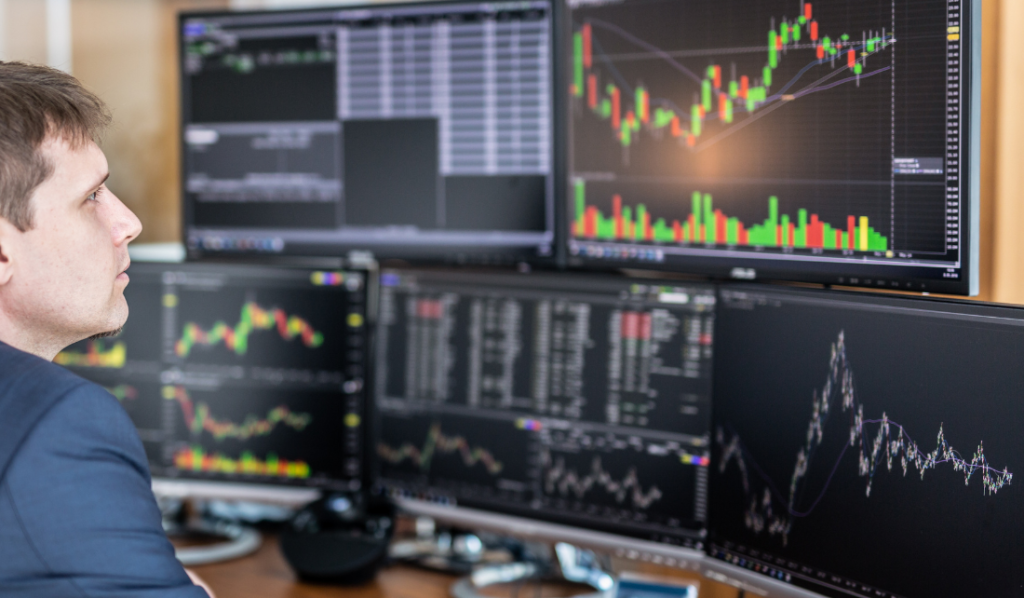 Homem analisando gráficos de investimentos em múltiplos monitores.